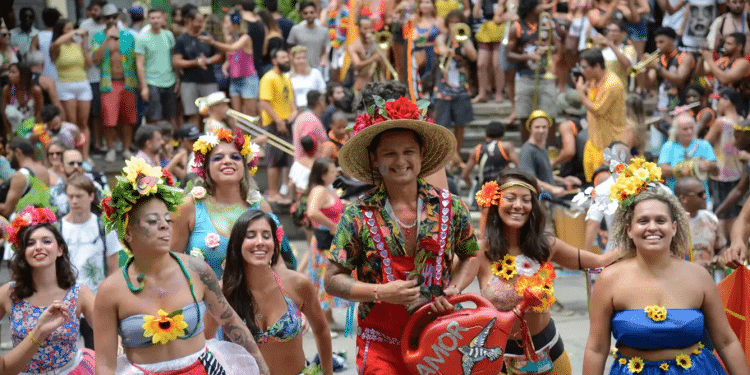 Grupo de foliões fantasiados com flores e adereços coloridos sorrindo durante bloco de Carnaval de rua