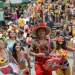 Grupo de foliões fantasiados com flores e adereços coloridos sorrindo durante bloco de Carnaval de rua