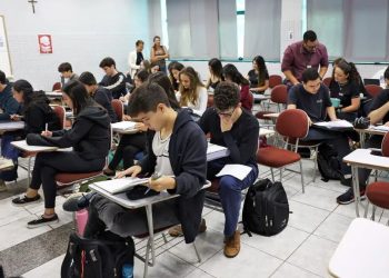 Fiscal acompanhando aplicação de prova em sala de aula com estudantes.