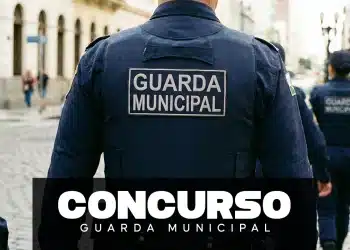 Agente da Guarda Municipal visto de costas durante patrulhamento urbano, com uniforme oficial identificado.