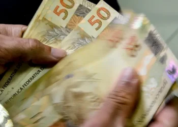 Notas de cinquenta reais sendo contadas, representando o benefício financeiro do novo programa do governo.