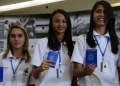 Três jovens sorridentes segurando carteira de trabalho azul e usando uniforme branco de trabalho