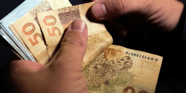 Mãos contando notas de 50 reais representando valores do programa Pé-de-Meia 2026.