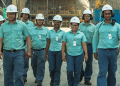 Equipe de funcionários da Vale caminhando em unidade industrial usando uniformes verdes e capacetes brancos.