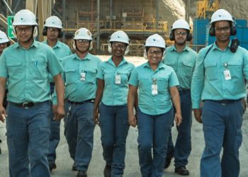 Equipe de funcionários da Vale caminhando em unidade industrial usando uniformes verdes e capacetes brancos.