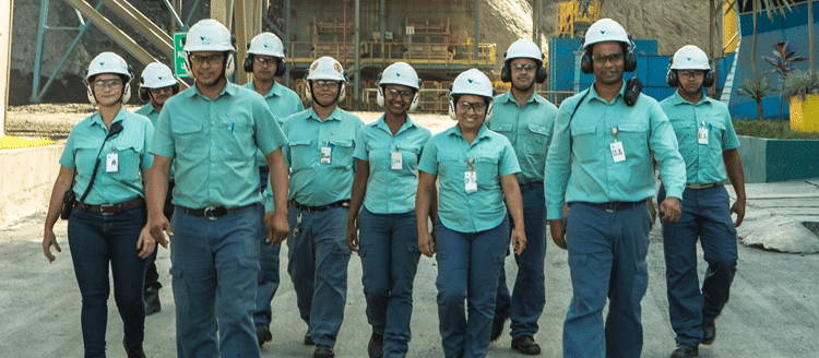 Equipe de funcionários da Vale caminhando em unidade industrial usando uniformes verdes e capacetes brancos.