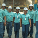 Equipe de funcionários da Vale caminhando em unidade industrial usando uniformes verdes e capacetes brancos.
