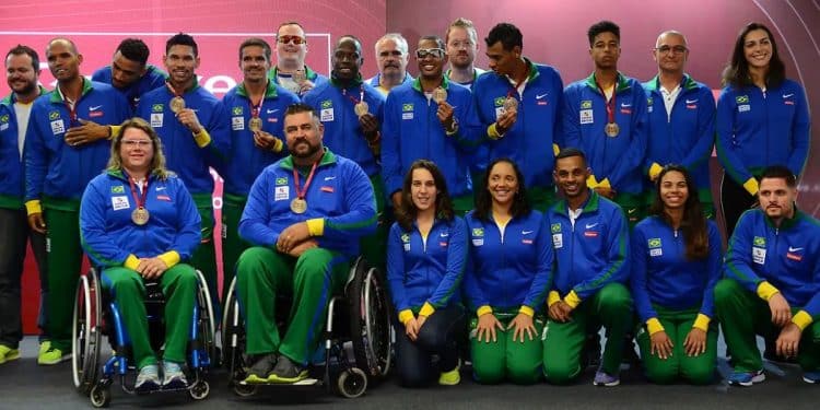 Grupo de atletas e paratletas da delegação brasileira vestindo uniformes oficiais azuis e verdes, alguns em cadeiras de rodas e outros em pé, exibindo suas medalhas de competição.
