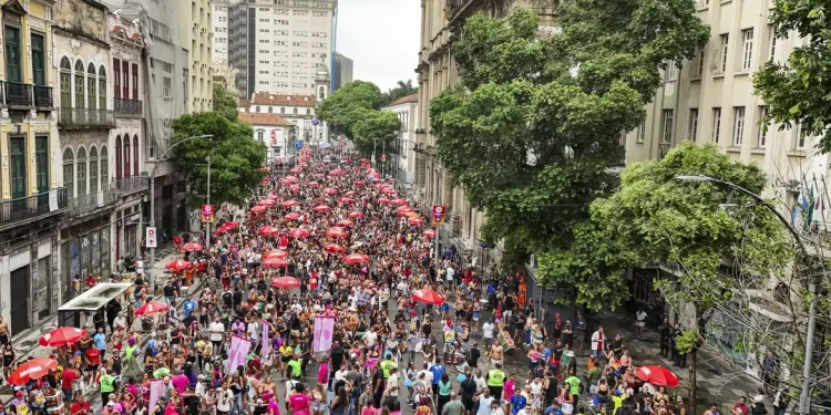 Multidão celebra Carnaval com blocos e guarda-sóis vermelhos nas ruas do Centro do Rio de Janeiro.