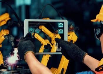 Operador controlando robôs industriais com tablet, utilizando inteligência artificial para otimização e automação dos processos de produção.