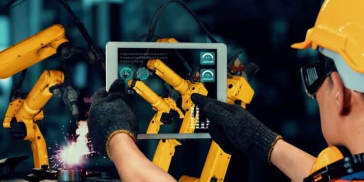 Operador controlando robôs industriais com tablet, utilizando inteligência artificial para otimização e automação dos processos de produção.