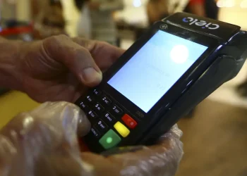 Mão com luva transparente usando máquina de cartão Cielo para pagamento