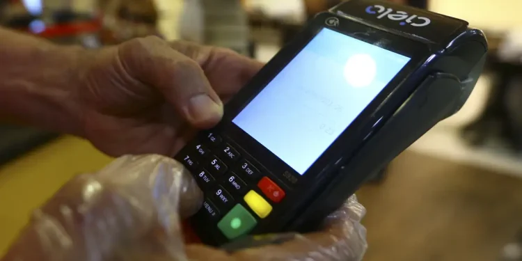 Mão com luva transparente usando máquina de cartão Cielo para pagamento