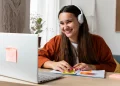 Mulher sorridente usando fones de ouvido, com laptop e post-its, simbolizando a aprendizagem e o desenvolvimento de habilidades com cursos online gratuitos.