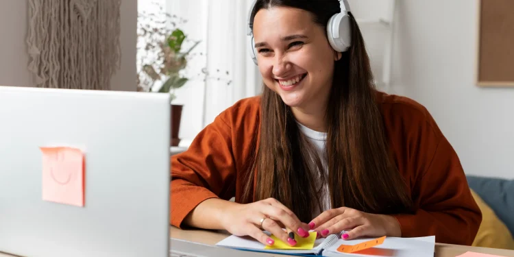 Mulher sorridente usando fones de ouvido, com laptop e post-its, simbolizando a aprendizagem e o desenvolvimento de habilidades com cursos online gratuitos.