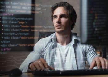 Jovem desenvolvedor de software concentrado trabalhando em frente a monitores com códigos de programação sobrepostos à imagem, representando carreiras de tecnologia de 2026.