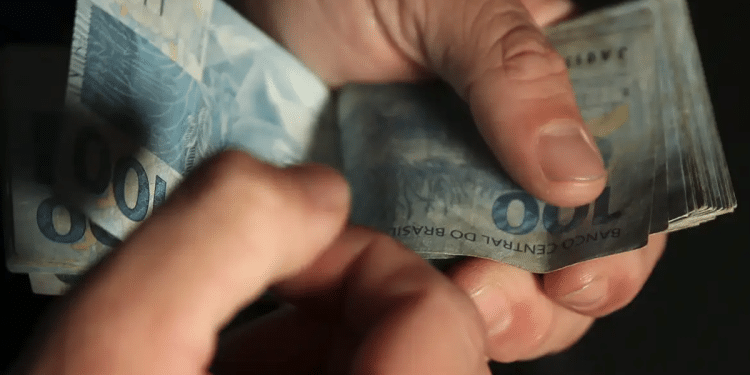 Mãos segurando e contando notas de 100 reais da moeda brasileira.