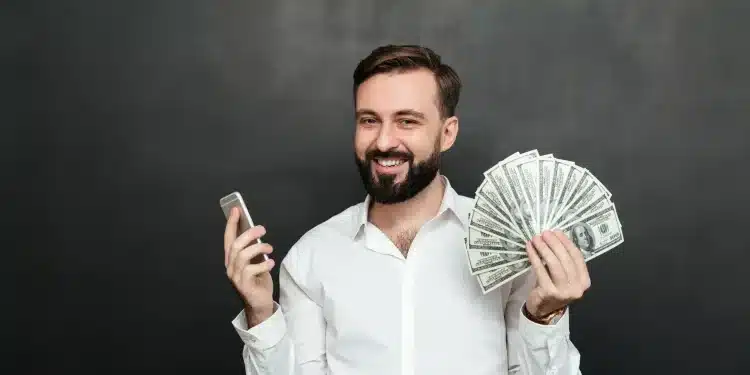Homem sorrindo enquanto segura um maço de dinheiro e um celular, simbolizando a conquista de um bom salário com oportunidades que não exigem diploma superior.