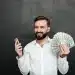 Homem sorrindo enquanto segura um maço de dinheiro e um celular, simbolizando a conquista de um bom salário com oportunidades que não exigem diploma superior.