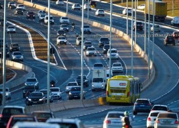 Vista aérea de uma rodovia movimentada com várias faixas repletas de carros, ônibus e motocicletas circulando sob a luz do entardecer.