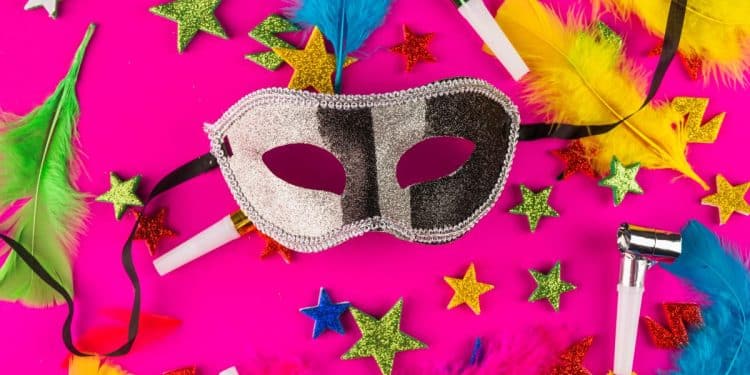 Uma máscara de Carnaval prateada e preta centralizada sobre um fundo rosa vibrante. Ao redor, há estrelas coloridas, penas verdes e amarelas, e apitos de festa espalhados.
