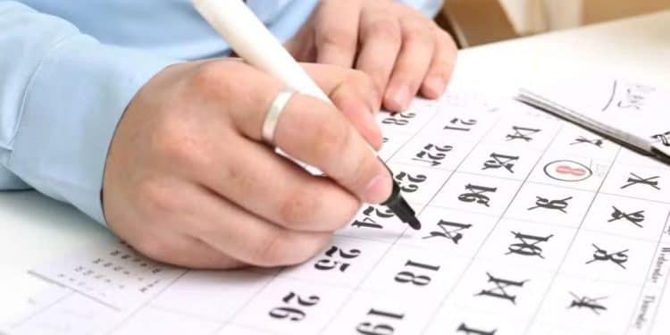 Pessoa marcando um dia no calendário com caneta, planejando os feriados de 2026.