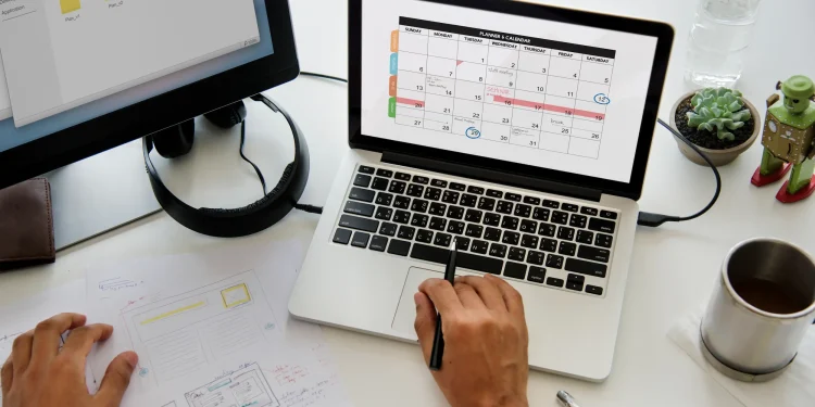 Pessoa organizando compromissos em um calendário mensal no notebook, ilustrando o planejamento de feriados prolongados em 2026.