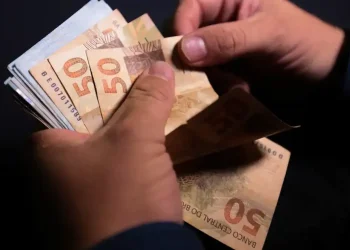 Mãos segurando notas de cinquenta reais representando aumento de pagamento do INSS e BPC em janeiro de 2026.