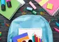 Mochila com materiais escolares coloridos sobre a mesa, representando itens comuns avaliados na lista de material escolar 2026.