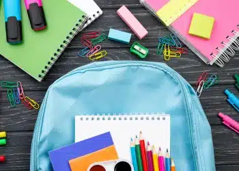 Mochila com materiais escolares coloridos sobre a mesa, representando itens comuns avaliados na lista de material escolar 2026.