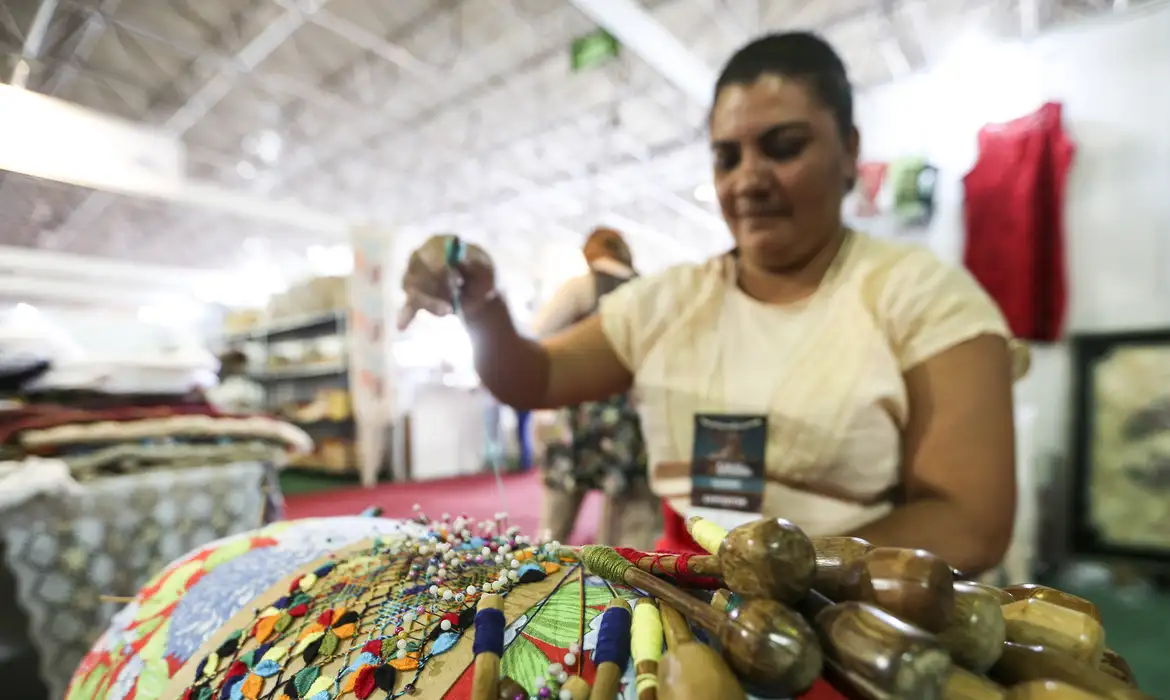 Artesã produz renda de bilro colorida usando bilros de madeira em mercado de artesanato