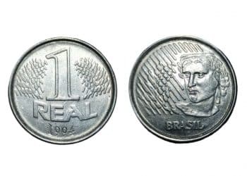 Visão frontal e dorsal da moeda original de 1 real de 1994, feita de aço inoxidável, exibindo o valor de face e a efígie da República.