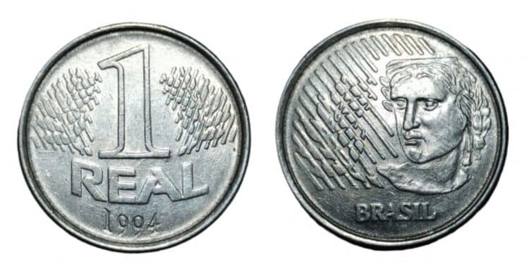 Visão frontal e dorsal da moeda original de 1 real de 1994, feita de aço inoxidável, exibindo o valor de face e a efígie da República.