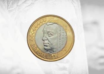 Visão frontal da moeda de 1 Real comemorativa do centenário de Juscelino Kubitschek, mostrando o perfil do ex-presidente no núcleo de prata e o anel dourado com a inscrição "BRASIL".