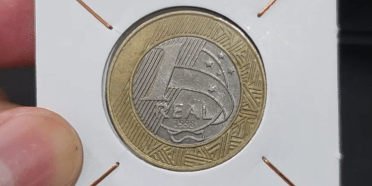 Close-up de uma moeda de 1 real de 1998 Direitos Humanos protegida em um suporte de papel branco para colecionadores.