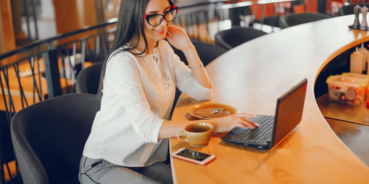 Profissional trabalhando remotamente em um café, com computador e xícara de café, representando uma profissão que pode pagar mais de R$ 10 mil por mês.