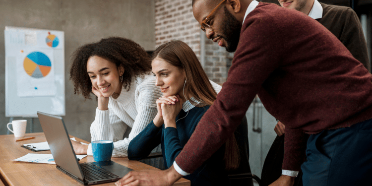 Quatro profissionais de diferentes etnias colaboram em frente a um laptop em ambiente de trabalho moderno.