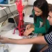 Duas pessoas montando uma prótese de mão robótica vermelha em laboratório de engenharia biomédica
