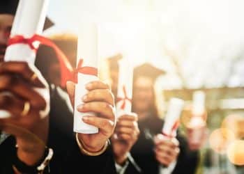 Grupo de formandos segurando seus diplomas, simbolizando a conquista do ensino superior, mas também os desafios de um mercado de trabalho competitivo.