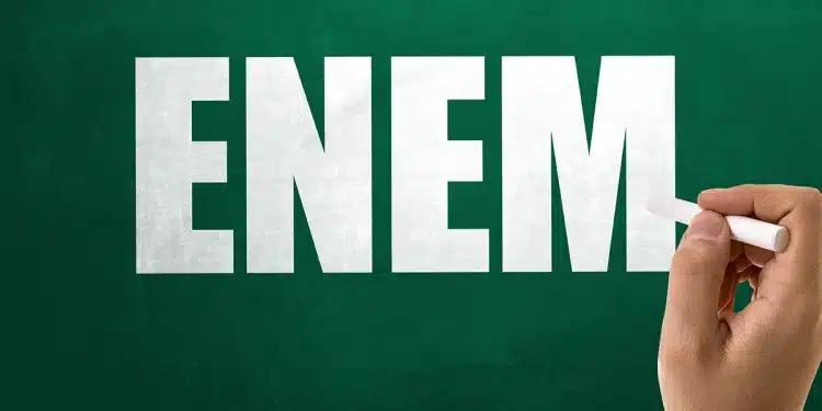 Mão escrevendo ENEM em quadro verde com giz, representando a prova nacional e o resultado da mesma que está disponível.