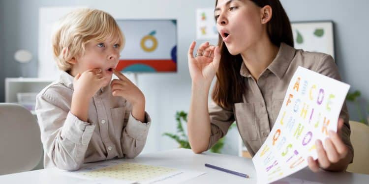 Fonoaudióloga mostrando exercícios orofaciais e um quadro de letras para uma criança, demonstrando o cuidado humano na terapia da fala.