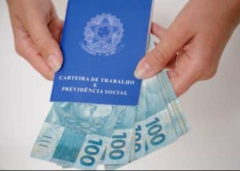 Carteira de Trabalho e Previdência Social sendo aberta junto a notas de R$ 100, ilustrando o tema do seguro-desemprego e benefícios trabalhistas.