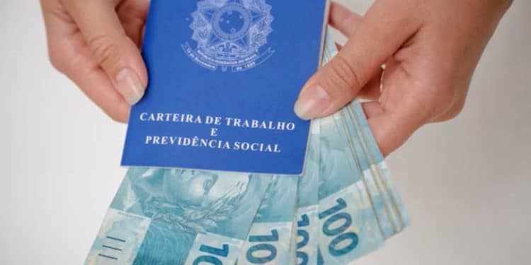 Carteira de Trabalho e Previdência Social sendo aberta junto a notas de R$ 100, ilustrando o tema do seguro-desemprego e benefícios trabalhistas.