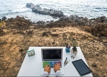 Pessoa trabalhando em um escritório improvisado à beira-mar, ilustrando o conceito de profissões que permitem viajar enquanto se trabalha.