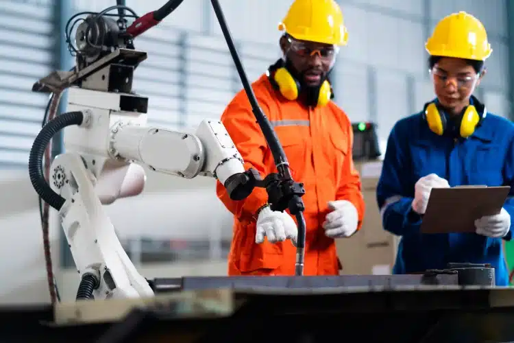 Trabalhador observando um robô realizar tarefas em uma linha de produção, simbolizando como a automação e a inteligência artificial podem impactar diversas profissões até 2030.