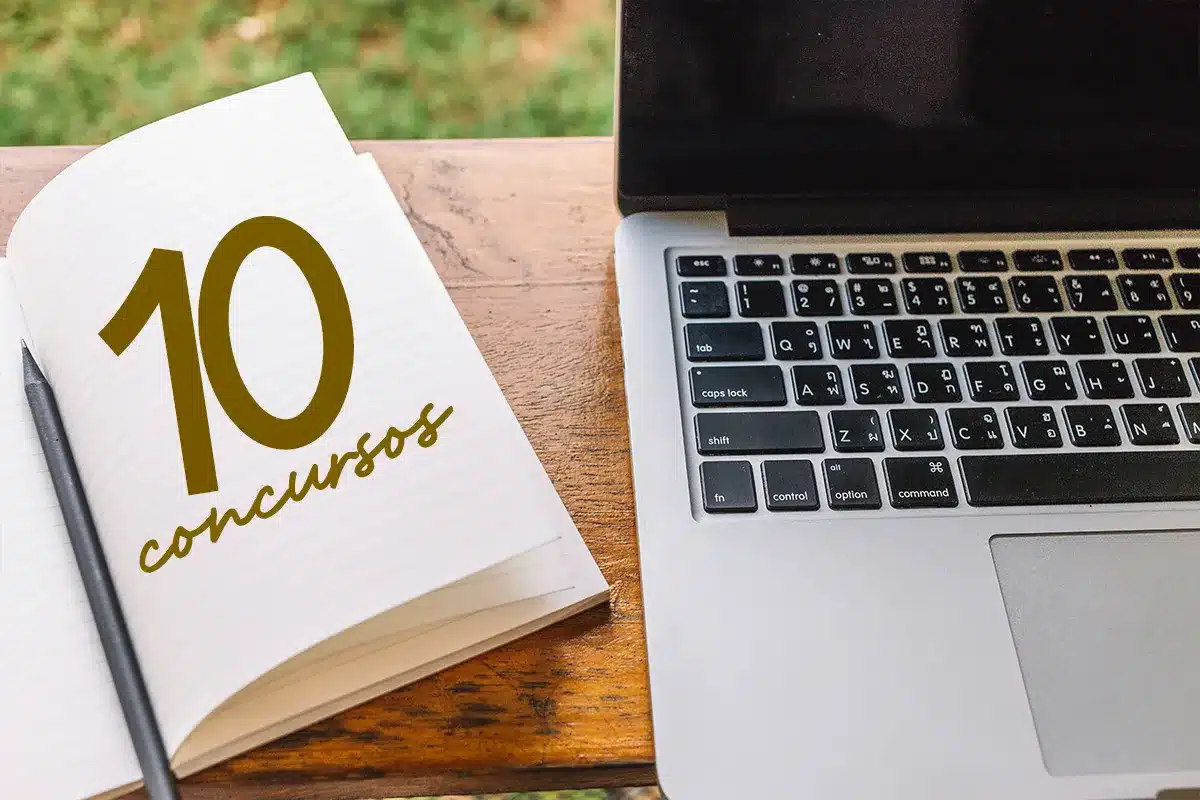 Caderno com “10 concursos” escrito e caneta ao lado de notebook sobre mesa de madeira.