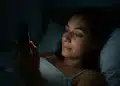 Mulher deitada na cama usando o celular à noite.