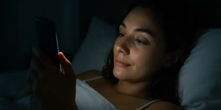 Mulher deitada na cama usando o celular à noite.