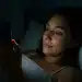 Mulher deitada na cama usando o celular à noite.