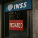 Placa vermelha escrito "fechado" pendurada na porta de unidade do INSS.